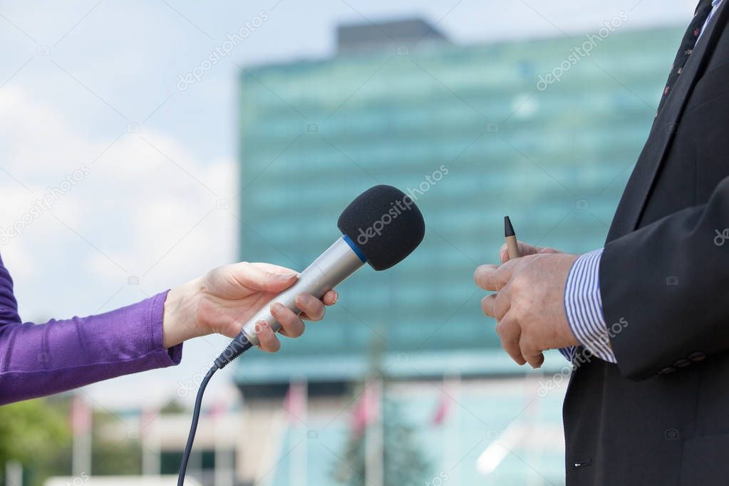 Female journalist interviewing businessman, corporate building in background