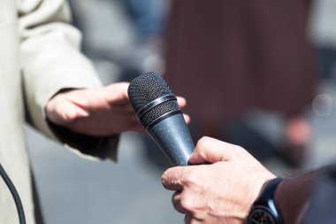 Gazeteci elinde mikrofon tutarak TV veya radyo röportajı yapıyor.