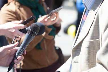 Gazeteci elinde mikrofon tutarak TV veya radyo röportajı yapıyor.