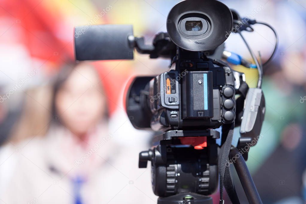 Video camera in the focus, blurred female reporter in the backgr