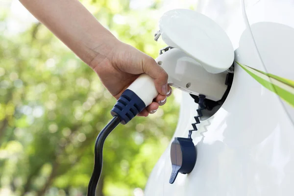 Mano sosteniendo un enchufe eléctrico para cargar el coche eléctrico. Desenfoque — Foto de Stock