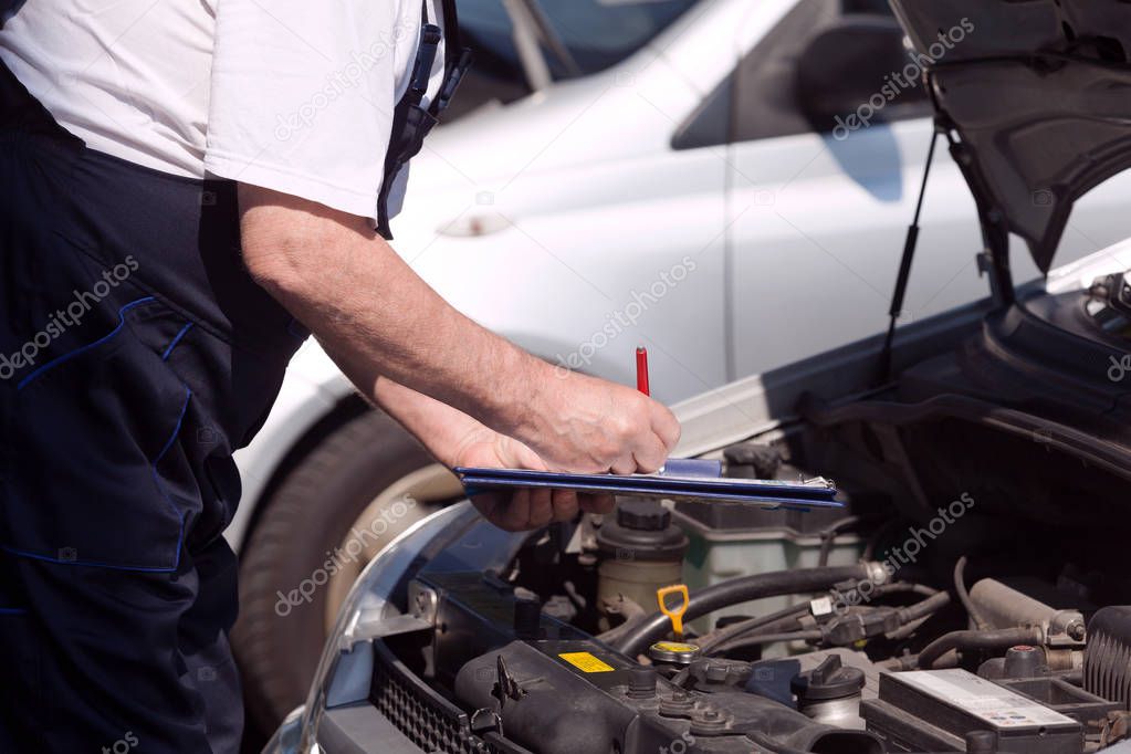 Car or motor mechanic checking a car engine and writing on the clipboard