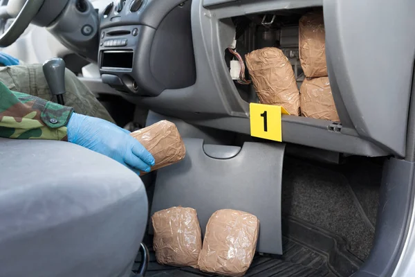 Oficial de policía sosteniendo paquete de drogas encontrado en compartimiento secreto de un coche — Foto de Stock