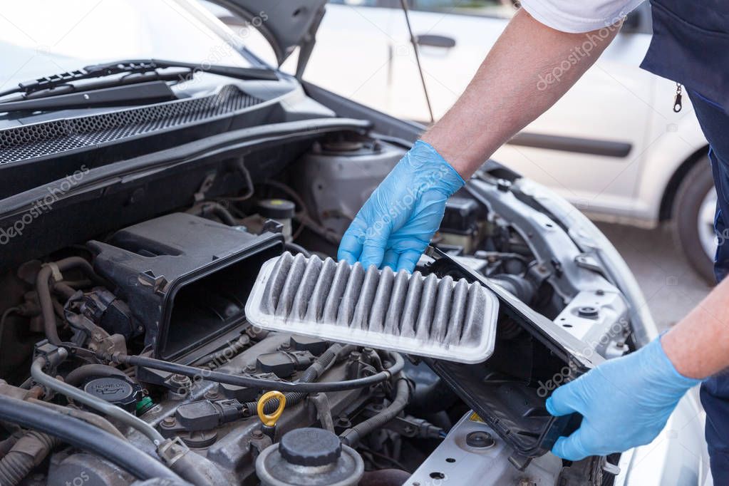 Auto mechanic wearing protective work gloves holds a dirty air filter