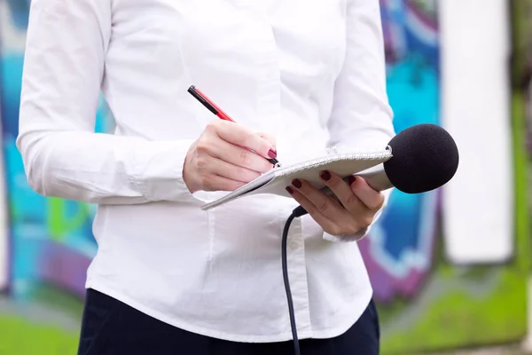Женщина-журналистка на пресс-конференции, пишет заметки, держит микрофон — стоковое фото