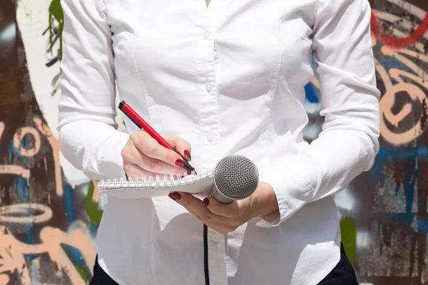 Female journalist at news event, writing notes, holding microphone — Stock Photo, Image