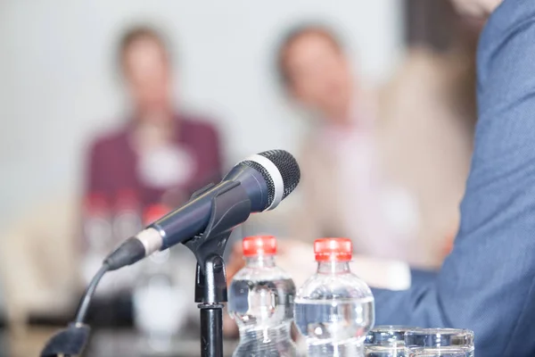 Microphone in focus against blurred people at roundtable event — Stock Photo, Image