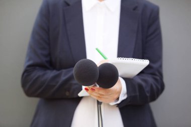 Basın konferansında ya da medya etkinliğinde çalışan gazeteci, mikrofon tutuyor ve notlar yazıyor