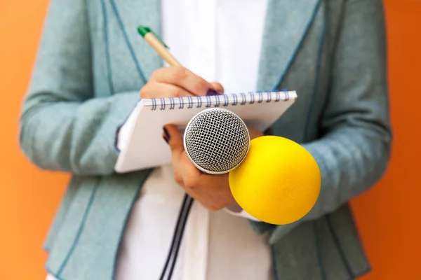 Woman journalist or reporter at press conference, writing notes, holding microphone. Journalism concept. — Stockfoto