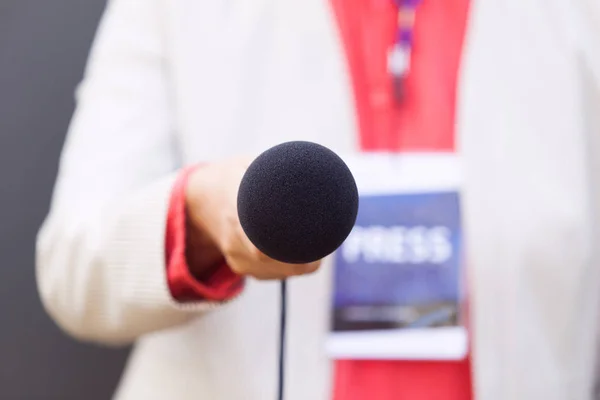 Female reporter holding microphone during media interview. Journalism concept.