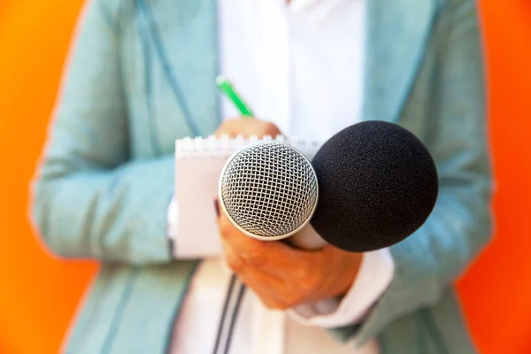 Female reporter at press conference or media event, writing notes, holding microphone