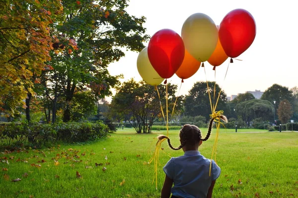 Девочка с косичками сидит на траве и смотрит на закат. Воздушные шары привязаны к косичкам девушки . — стоковое фото