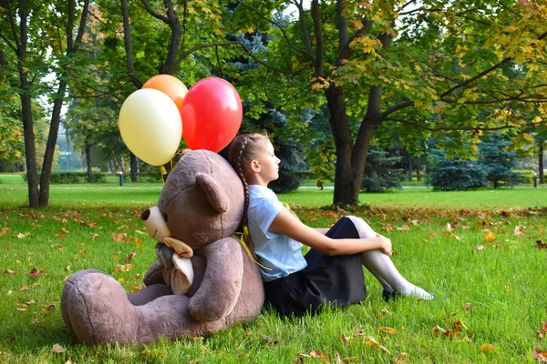 Грустная девочка с большим плюшевым мишкой и воздушными шариками в парке. Проблемы подростков в школе . — стоковое фото