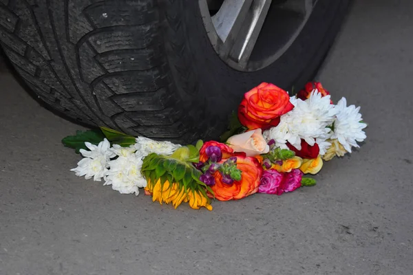 A bouquet of flowers under the wheel of a car. Crushed and broken love. — Stock Photo, Image