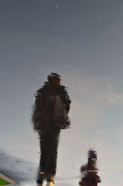 Islak kaldırımdaki insanların karanlık gölgeleri. İnsan siluetleri ıslak yola yansıyor.