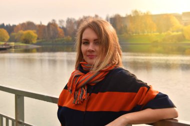 Sonbahar montu giymiş sarışın bir kadın gezinti güvertesinde duruyor..