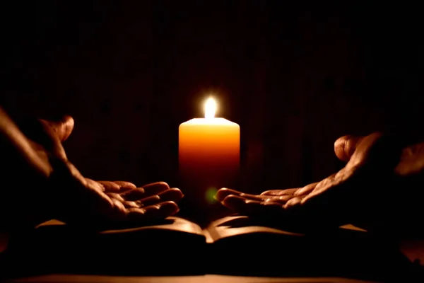 在黑暗中点着蜡烛进行宗教祈祷 求神的帮助 在圣经里祈祷 关于黑色背景的旧书的掌心 蜡烛和手 女人在黑暗中祈祷 晚上读经 — 图库照片