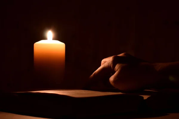 Karanlıkta mum eşliğinde İncil okuyor. Geceleyin parmak kitaptaki gibi. Biri karanlıkta gizemli bir kitap okuyor. — Stok fotoğraf