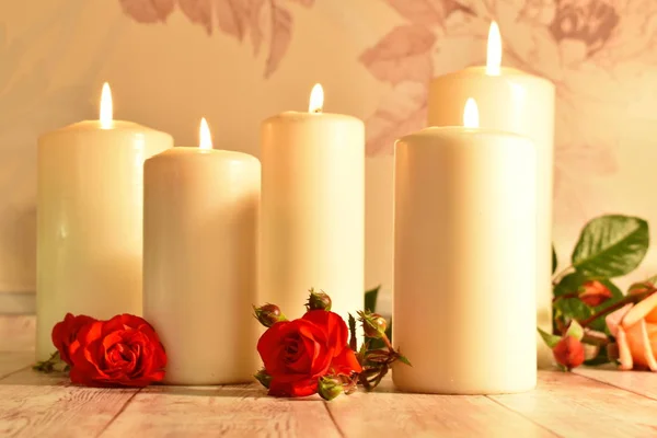 White candles and red rose buds on a wooden. Health and personal care concept.