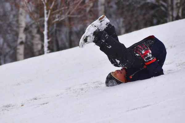 El chico está rodando montaña abajo en invierno sobre su espalda. Niño cae de deslizamiento de nieve . —  Fotos de Stock