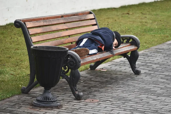 Бездомный мальчик спит на скамейке в парке. Подросток лежит на скамейке в холоде . — стоковое фото