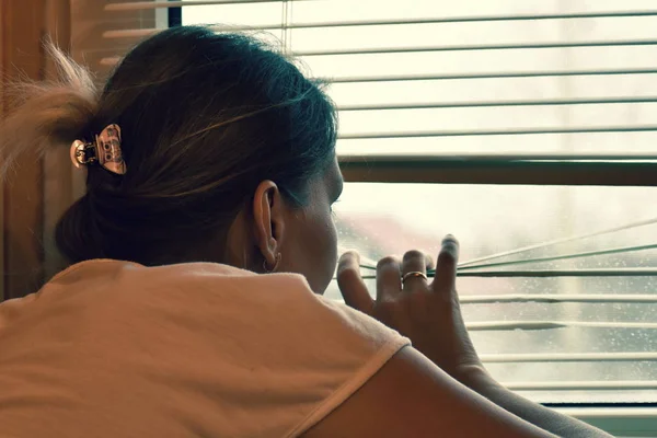 Seorang wanita mengintip keluar jendela melalui tirai . — Stok Foto