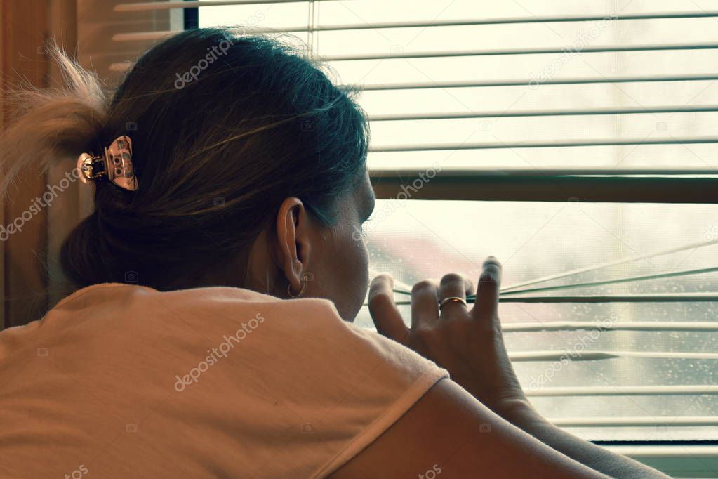 A woman peeps out the window through the blinds.