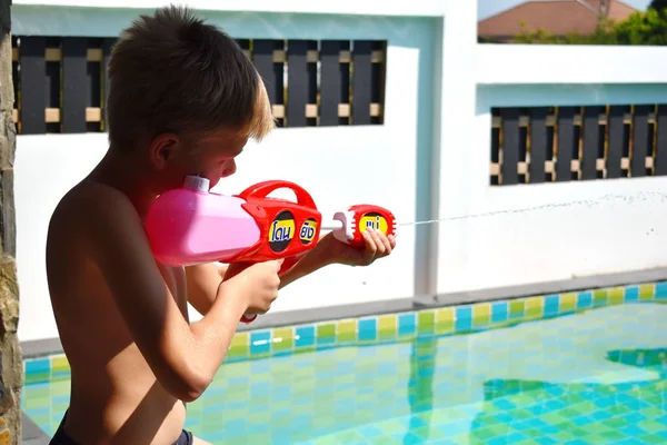 Ragazzo bambino spara con una pistola ad acqua. Giochi attivi in acqua in piscina . — Foto Stock