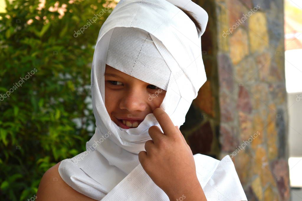 A child in a mummy costume. The boy wrapped himself in toilet paper. A little boy is playing mummy