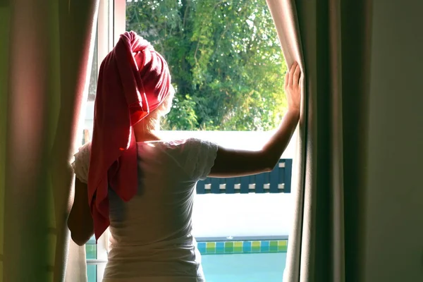 Dziewczyna z ręcznikiem na głowie patrzy przez okno. Początek dobrego dnia.. — Zdjęcie stockowe