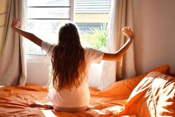 Het meisje wordt gelukkig wakker in de ochtend. Zonlicht valt op het gezicht van de tiener. — Stockfoto