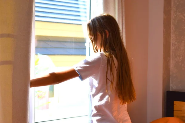 Een meisje wordt wakker bij het raam in de ochtend. Fijne zonnige ochtend. — Stockfoto