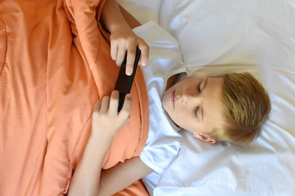 Мальчик-подросток играет по телефону в постели. Детская мобильная зависимость — стоковое фото