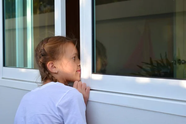 Seorang gadis kecil mengintip melalui jendela. Anak perempuan melihat ke luar jendela — Stok Foto