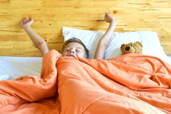 De jongen wordt 's morgens wakker in bed. Stretch in de ochtend handen. — Stockfoto