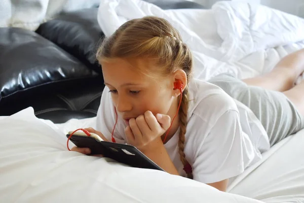 Дівчинка-підліток дивиться по телефону. Дівчина слухає музику на навушниках у ліжку . — стокове фото