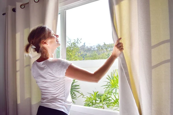 Bella ragazza che guarda fuori dalla finestra. La donna alla finestra. Una calda giornata di sole . — Foto Stock