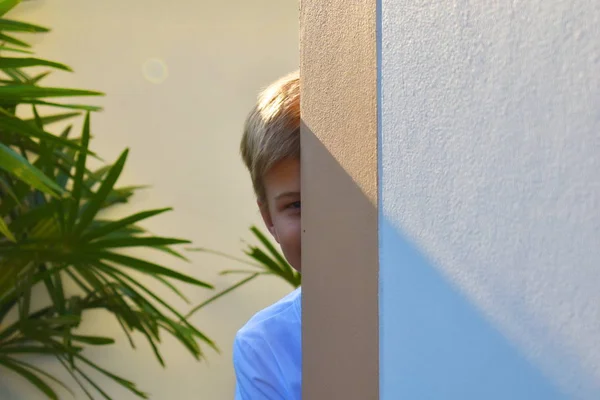 Un garçon regarde par derrière la maison. L'enfant espionne doucement. Cache-cache . — Photo