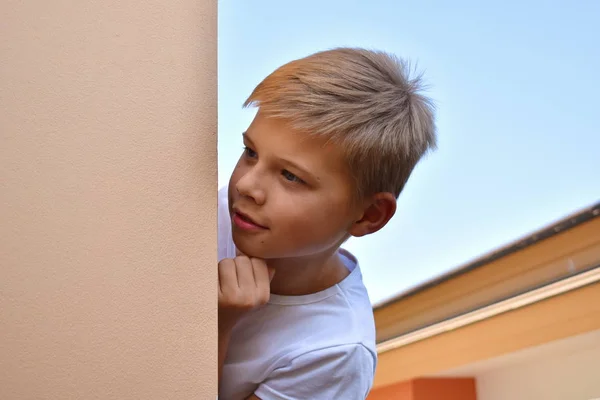 A boy looks out from behind the house. The child slyly peeping. Hide-and-seek. — 스톡 사진