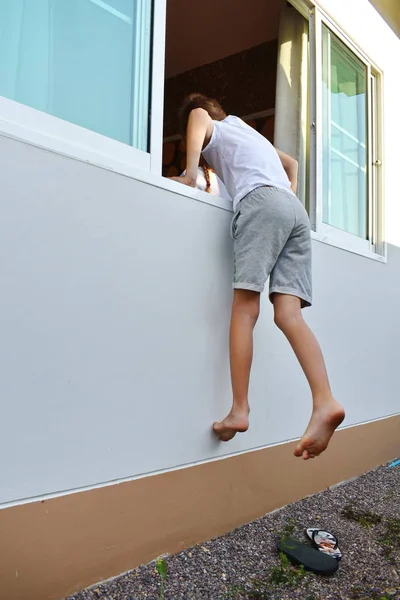 Anak itu memanjat lewat jendela. Anak itu menyelinap di jendela yang terbuka. bersembunyi dan mencari di luar ruangan. Permainan anak-anak yang menyenangkan . — Stok Foto