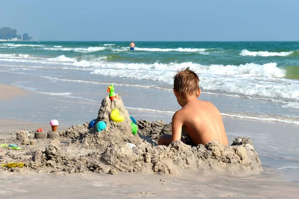 Pojken leker i sand på stranden. Barnet bygger ett sandslott. En semester på havet. Sommarsemester i tropikerna. Leksaker för barn — Stockfoto
