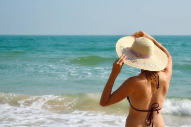 Denizdeki şapkalı kız. Denize bakan güzel bir kadın. Arkadan manzara. Okyanusta rahatla. Tropik bölgelerde tatil.