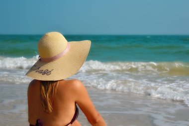 Denizdeki şapkalı kız. Denize bakan güzel bir kadın. Arkadan manzara. Okyanusta rahatla. Tropik bölgelerde tatil.