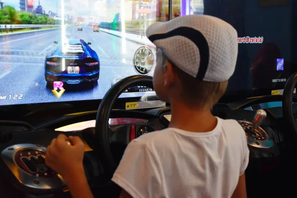 Tailandia. Hua hin. Enero 2020. Un chico juega juegos de ordenador en el centro comercial. simulador de juegos de máquina. Juego de carreras de coches con la rueda . —  Fotos de Stock
