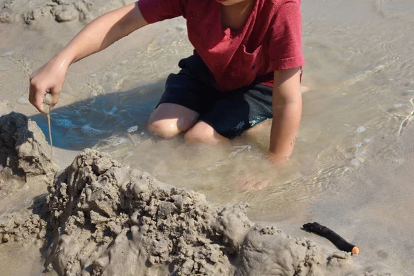Ein Junge spielt in einer Pfütze am Strand. Das Kind sitzt in einer Pfütze im Sand. fröhlicher lustiger Sommer. — Stockfoto