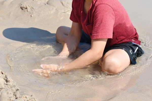 Een jongen speelt in een plas op het strand. Het kind zit in een plas in het zand. Gelukkige grappige zomer. — Stockfoto