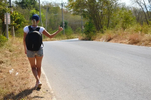 Schöne Mädchen fängt das Auto auf der Straße. Touristen mit Rucksack stehen im Sommer auf der Straße. Autostopem allein. — Stockfoto