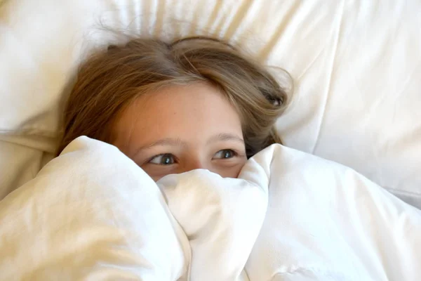 Милая девочка, улыбающаяся в постели. Счастливый милый ребенок в постели. Дом на рассвете. Портрет маленькой девочки на одеяле . — стоковое фото
