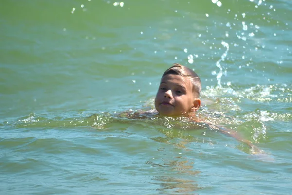 Chłopiec pływa w morzu. Chłopak pływa w otwartym oceanie. Uczę się pływać w słonym morzu. Wakacje w tropikach. — Zdjęcie stockowe