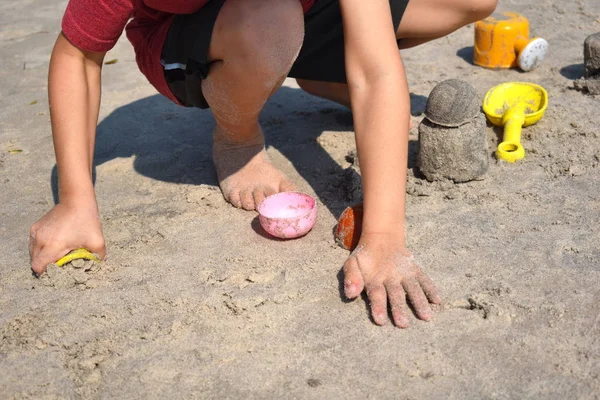 Ein Junge spielt am Strand im Sand. das Kind baut Sandfiguren. Spielzeug am Strand. frohe Feiertage am Meer. — Stockfoto